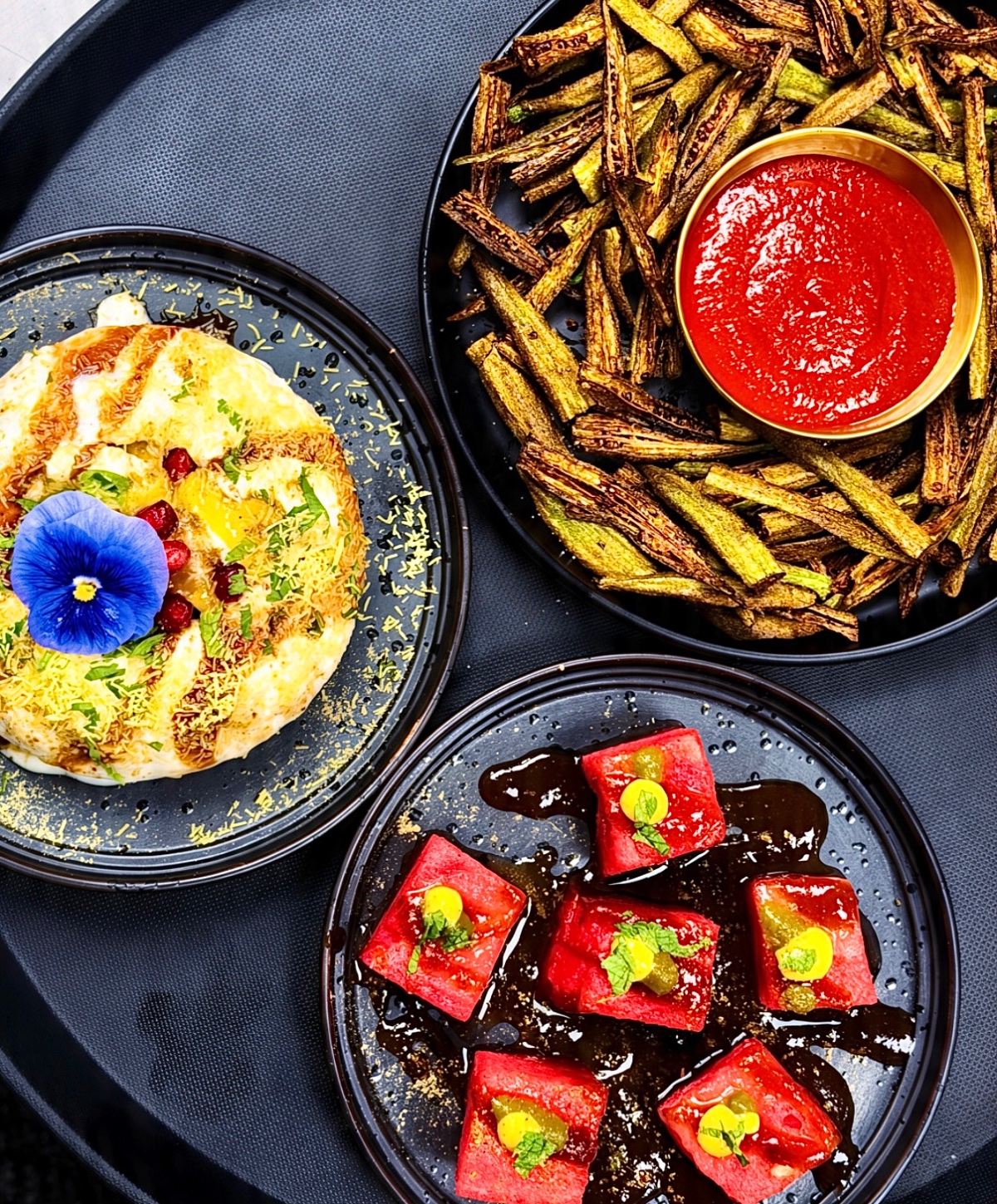 Raj Kachori, gunpowder okra chaat and watermelon chaat on black plates