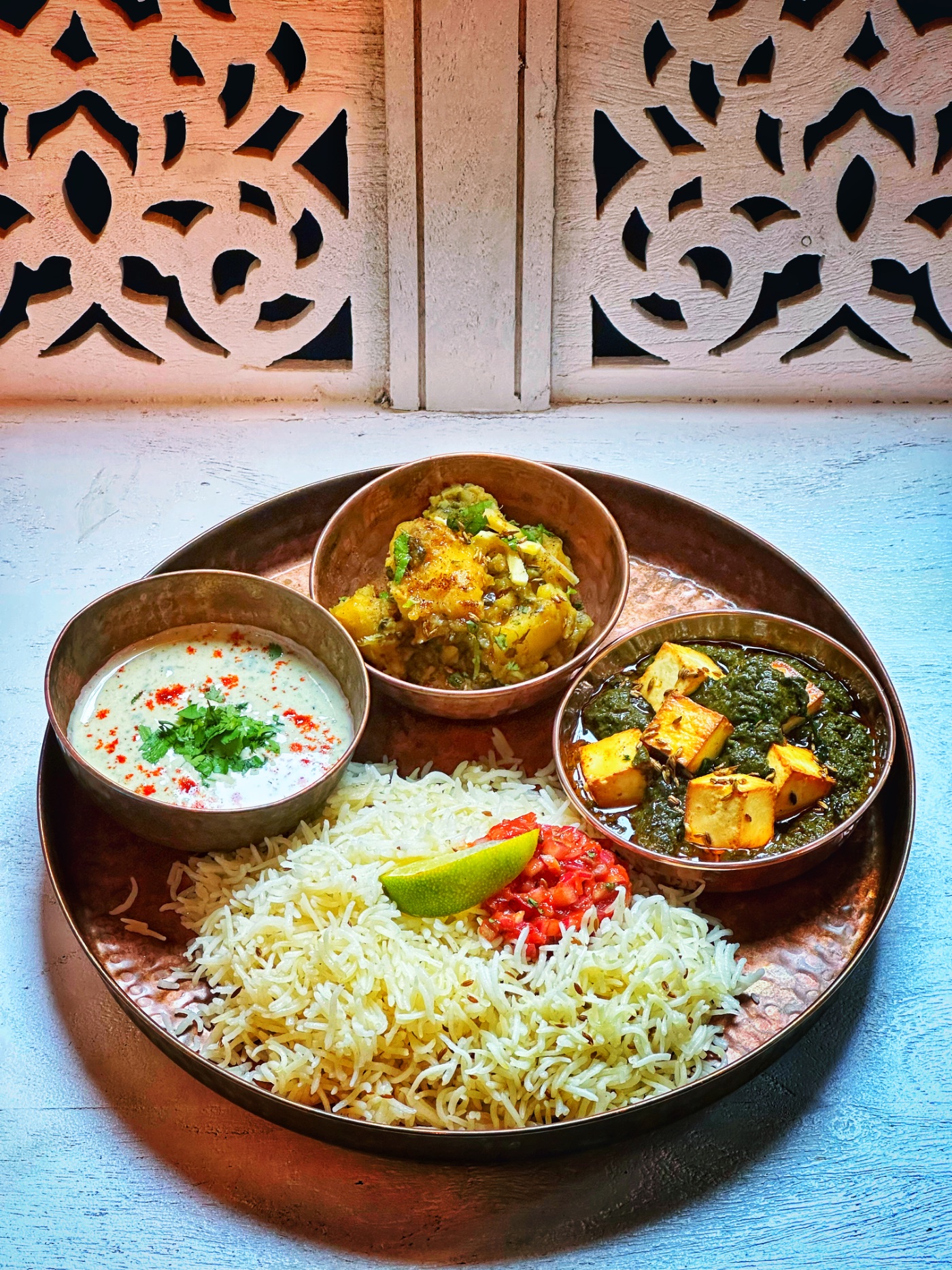Punjabi thali: palak paneer, methi aloo, raita and rice on a copper platter